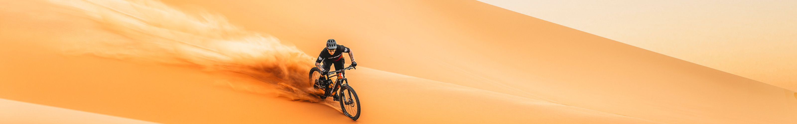 Pilotage engagé d'un rider équipement complet sur VTT Mondraker tout-suspendu en virage serré soulevant de la poussière